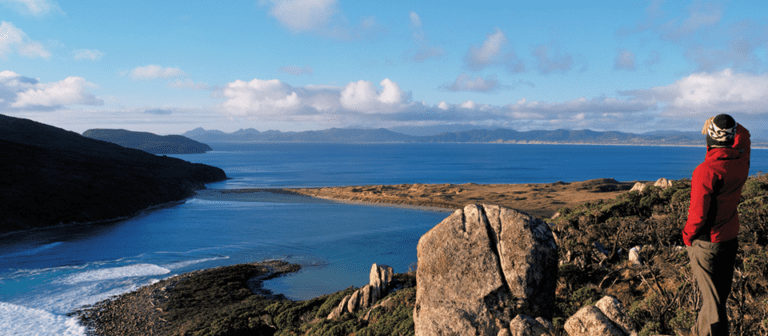 מטייל עומד מעל חוף פראי במסלול ראקיורה טרק ומביט אל האוקיינוס והאיים הרחוקים