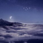 צביר כוכבי המטאריקי בוהק בשמי לילה סגולים מעל ים של עננים לבנים ופסגות הרים מושלגות בניו זילנד, כשהסהר של הירח מאיר ברקע.