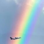 AIRNZ מטוס טס דרך קשת בענן בשמי ניו זילנד מעל נוף הררי