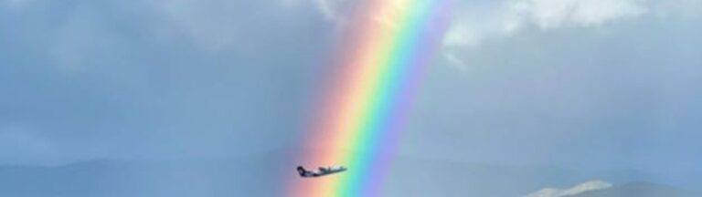 AIRNZ מטוס טס דרך קשת בענן בשמי ניו זילנד מעל נוף הררי