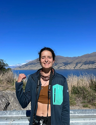מטיילת מחייכת ליד אגם והרים בניו זילנד