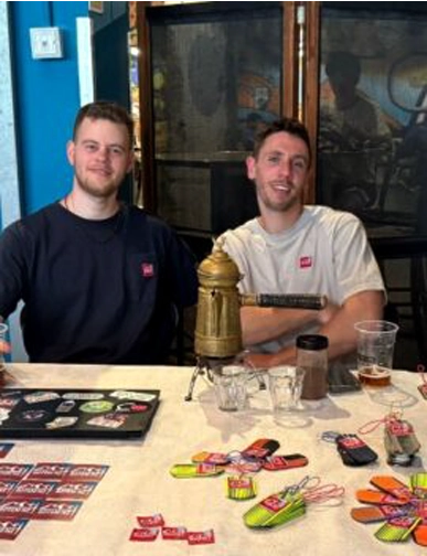 יונתן ואופיר מצוות Rotem NZ בדוכן שיווק בכנס מטיילים עם חומרי פרסום על השולחן