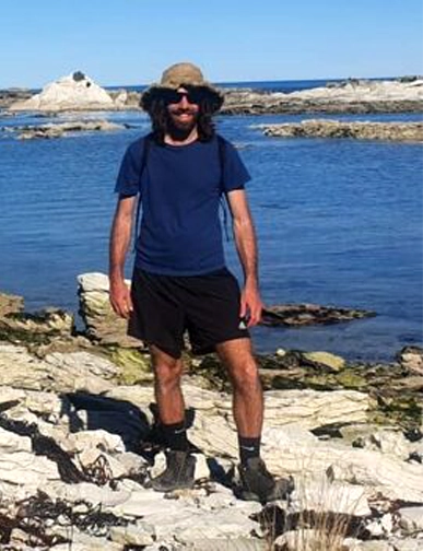 גבר עומד על חוף סלעי ליד ים כחול בניו זילנד