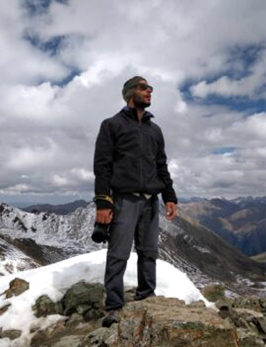 רון מצוות Rotem NZ עומד על פסגת הר מושלגת עם נוף הררי דרמטי בניו זילנד